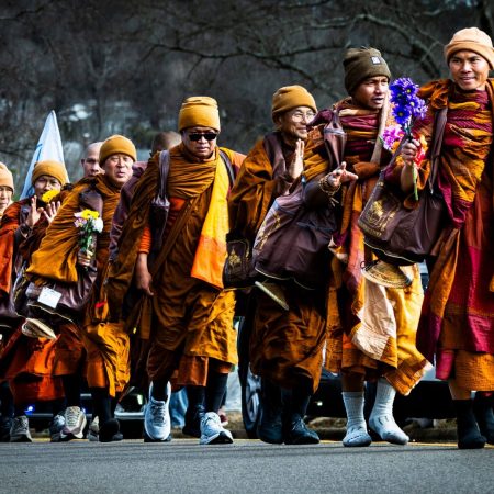 Monks walking in road wearing orange robes and carrying personal items