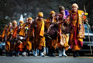 Monks walking in road wearing orange robes and carrying personal items